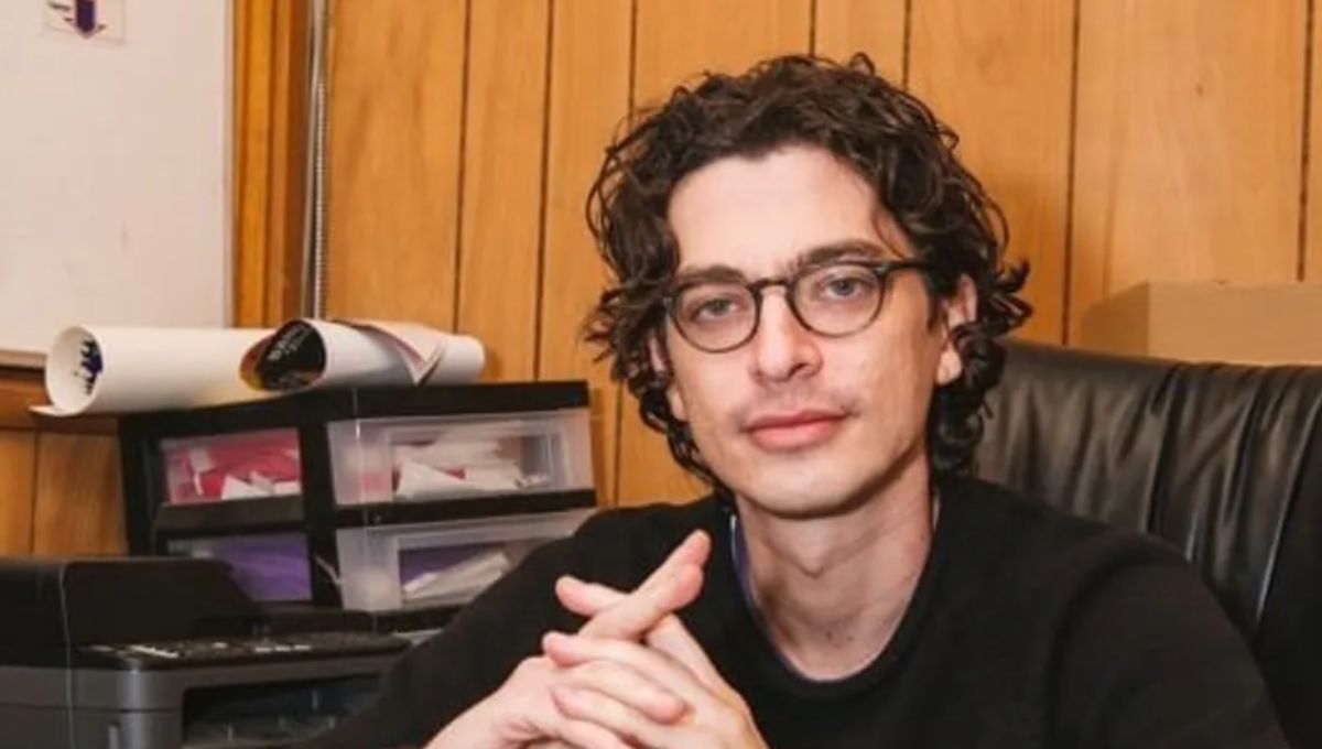 Adam Friedland seated at a retro talk-show desk with a city-light backdrop