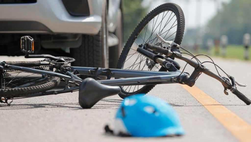 Cyclist’s helmet, cracked visor, and action camera sitting beside a scuffed bike wheel after a crash
