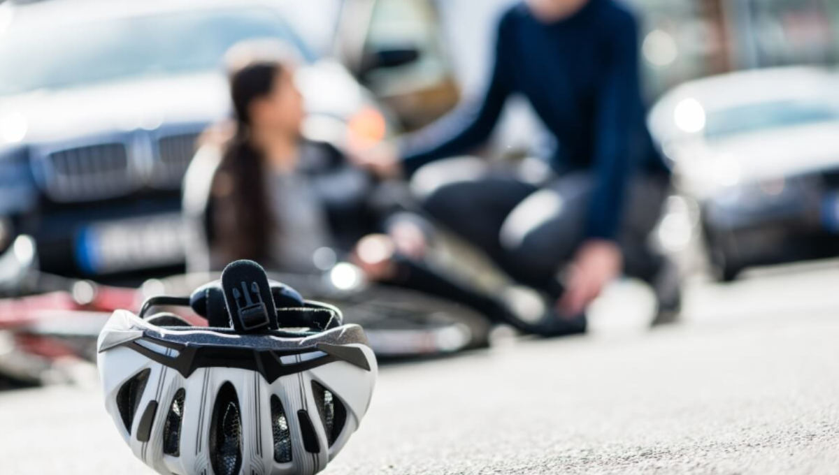 Cyclist’s helmet, cracked visor, and action camera sitting beside a scuffed bike wheel after a crash
