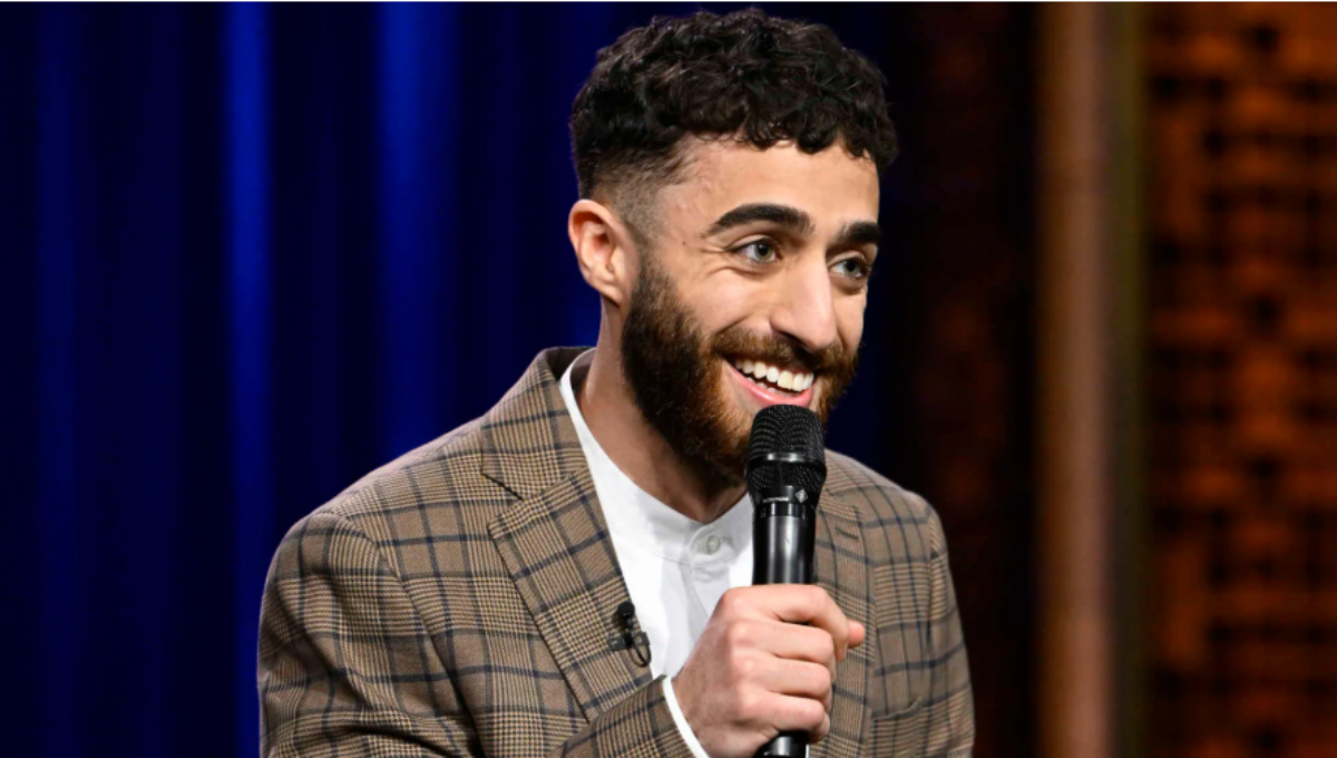 Comedian Emil Wakim on stage holding a microphone under warm spotlight
