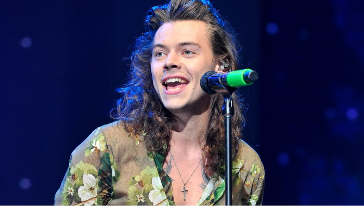 Harry Styles performing on stage in a sequined jumpsuit under warm spotlights
