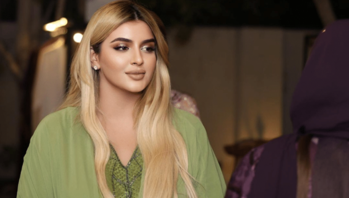 Sheikha Mahra at a fashion event, photographed in a gold-toned dress with a soft spotlight