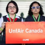Air Canada flight attendant picketing outside the terminal with a stop sign demanding fair pay in 2025
