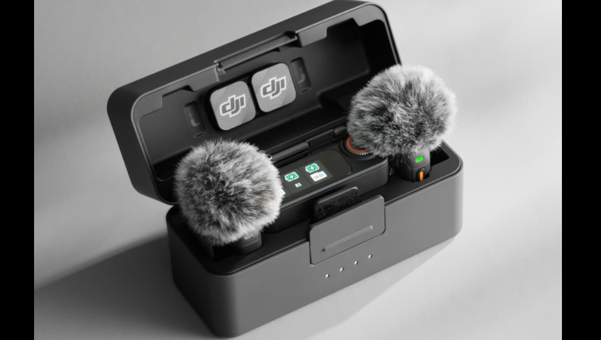 DJI Mic 3 transmitter, receiver, and charging case on a desk with camera gear in the background