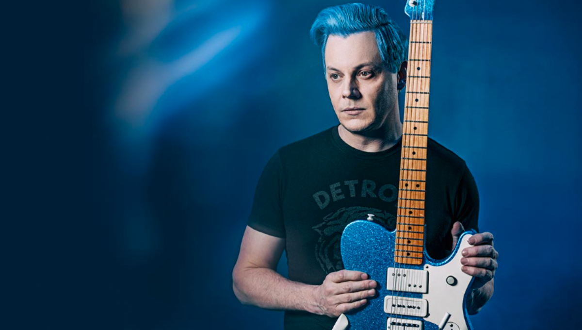 Jack White performing onstage with a blue-lit guitar at a packed festival