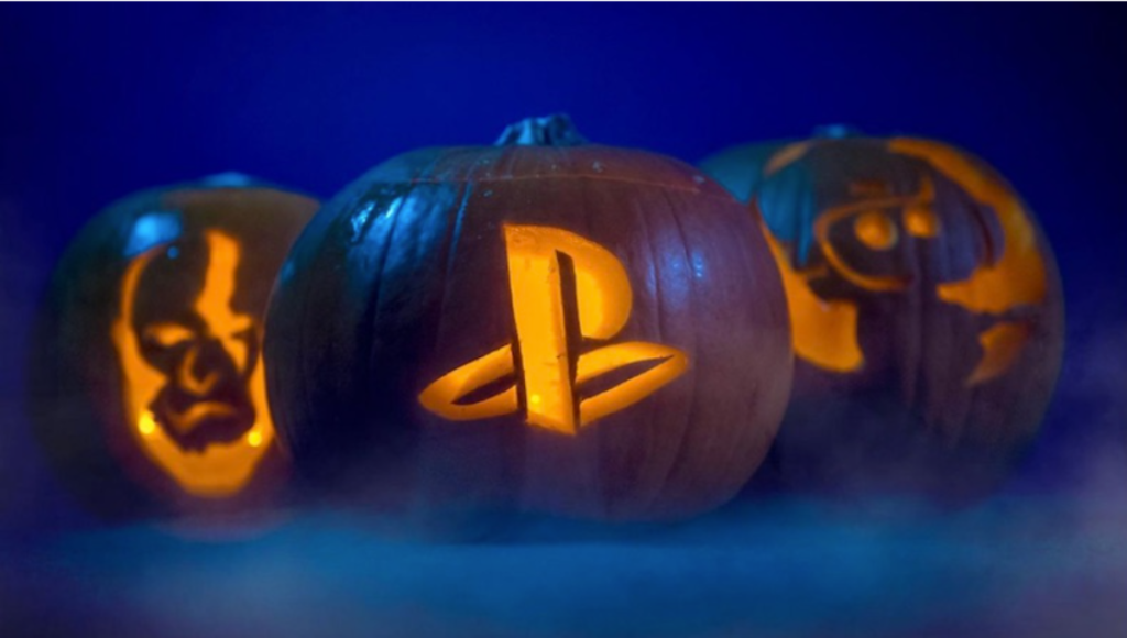 A DualSense controller lit by orange and purple Halloween lights next to a PS5 console