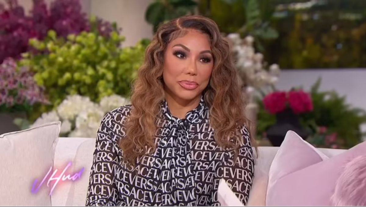 Tamar Braxton on stage in a spotlight, hand on mic, with a serious expression