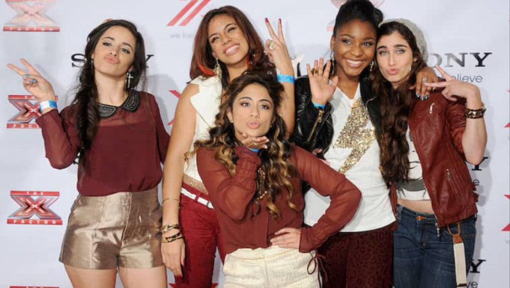 Fifth Harmony members on stage in coordinated black outfits performing under spotlights