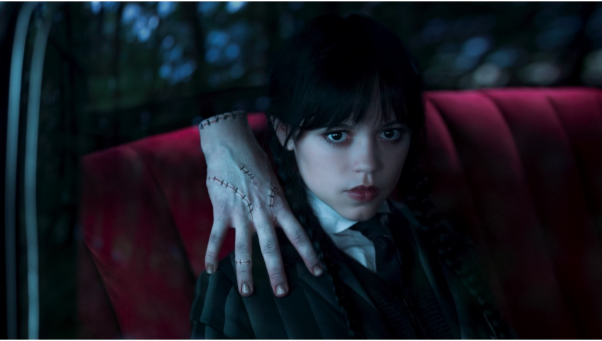 Jenna Ortega as Wednesday Addams staring forward in a gothic academy hallway, symbolic of a new season