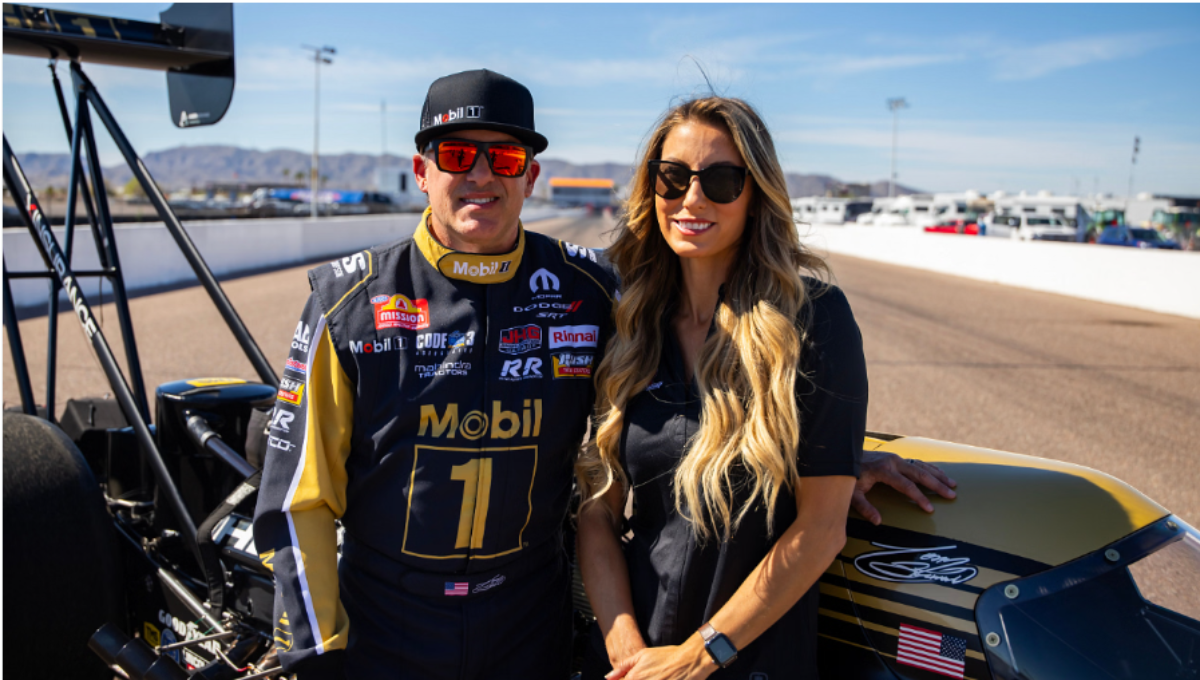 Leah Pruett beside a Tony Stewart Racing Top Fuel dragster during a 2025 test day, helmet in hand, crew working in the background