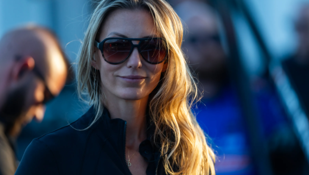 Leah Pruett beside a Tony Stewart Racing Top Fuel dragster during a 2025 test day, helmet in hand, crew working in the background