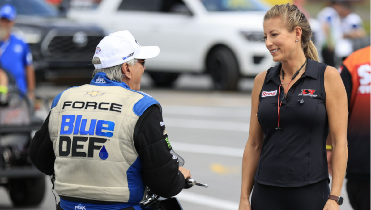 Leah Pruett beside a Tony Stewart Racing Top Fuel dragster during a 2025 test day, helmet in hand, crew working in the background