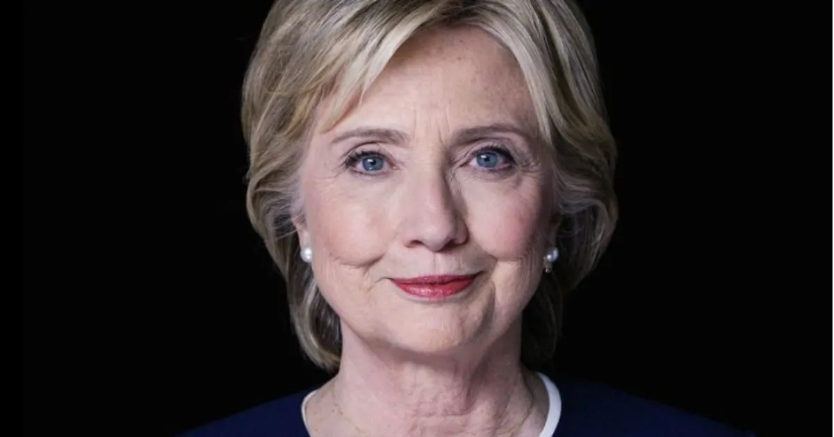 Hillary Clinton speaking at a policy forum with a blue backdrop and audience silhouettes