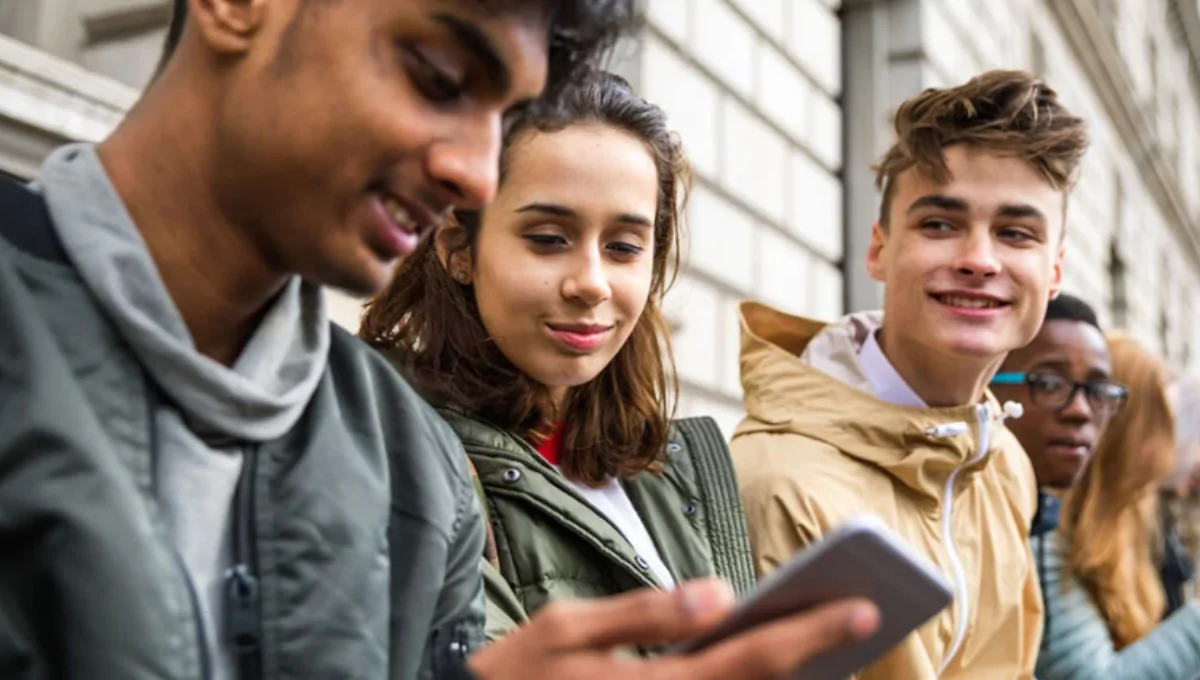 A diverse group of Gen Z students using smartphones and laptops in a bright campus commons